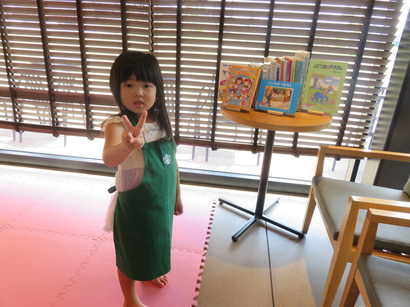 スターバックスコーヒーのこども用エプロンを着用して本の隣でポーズを取るお子さんの写真