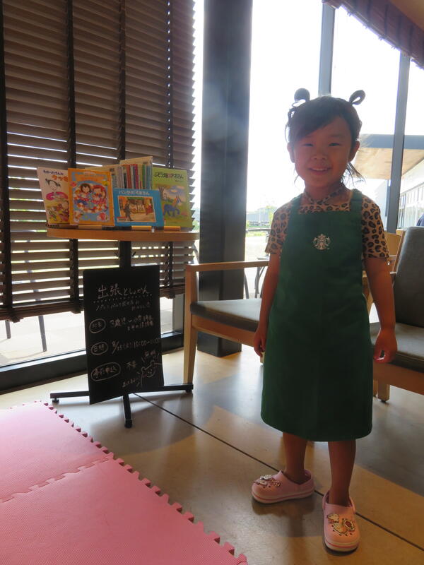 スターバックスコーヒーのこども用エプロンを着用して本の隣に立つお子さんの写真